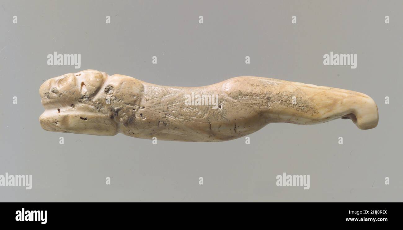 Amulett in Form eines Löwen mit ausgestreckten Beinen ca. 3300–2900 v. Chr. Dieses kleine Objekt, das aus einem Muschelstück geschnitzt wurde, zeigt einen Löwen im Spagat, mit vollständig ausgestreckten Hinterbeinen und gebeugten Vorderbeinen zum Kopf hin. Alle Merkmale, einschließlich des Kopfes, sind nur rudimentär modelliert und fast vollständig detaillos. Stattdessen betonte der Schnitzer die dreidimensionale Form des Tieres: Zwei Schwellungen deuten auf die Schulter und den Hackel hin, verbunden durch einen Körper, dessen Kurve die dynamische Bewegung des Tieres unterstreicht. Die Formen der Beine sind blockartig und die Eigenschaften des Kopfes schwierig Stockfoto