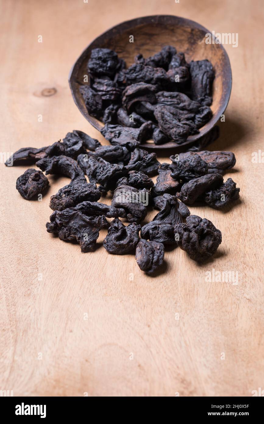 Sonnengetrocknete Garcinia-Früchte, die auf einer hölzernen Tischplatte verstreut sind, schwarz geschrumpfte Aromakräuter aus südasien, auch bekannt als brindlige Beere, Goraka oder Stockfoto