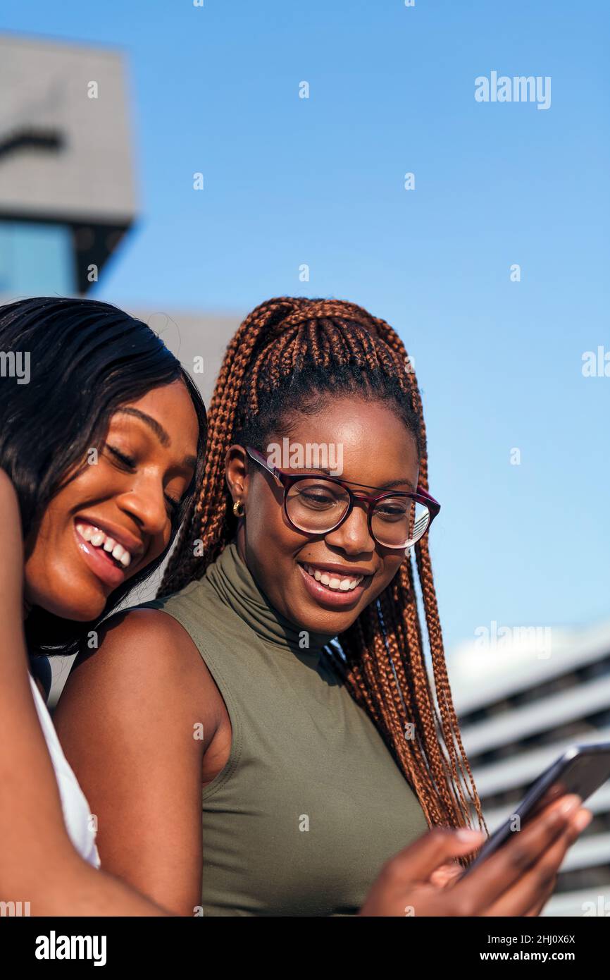 Vertikales Foto von zwei jungen schwarzen Frauen, die lächeln und Spaß am Handy haben, Konzept der Jugend und Kommunikationstechnik, Kopierraum fo Stockfoto