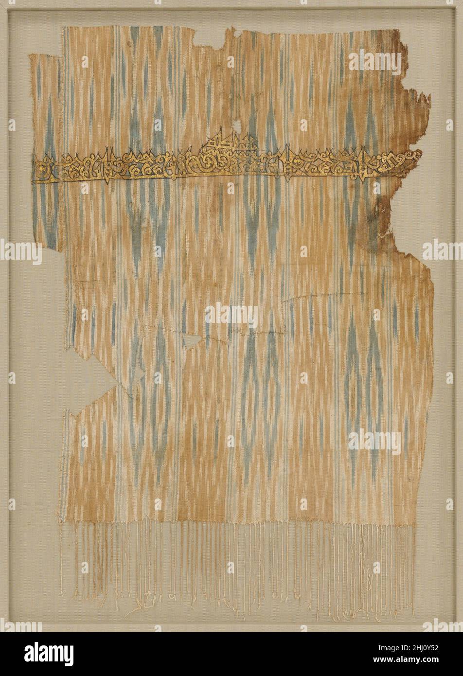 Tiraz Textile Fragment Ende des 9th.–Anfang des 10th. Jahrhunderts die gestreiften Textilien des Jemen waren in der gesamten islamischen Welt berühmt. Sie wurden in der Resist‑dyed ikat-Technik hergestellt, um Muster aus Pfeilspitzen und Diamanten zu bilden. Inschriften auf jemenitischen Ikaten werden häufig gemalt, wie in diesem Beispiel. Solche beschrifteten Textilien wurden tiraz genannt, vom persischen Wort, das 'Stickerei' bedeutet. Sie wurden in Tiraz-Werkstätten unter königlicher Kontrolle hergestellt. Solche Textilien trugen in der Regel Inschriften mit der Bezeichnung des aktuellen Lineals oder Kalifen, dem der Empfänger Loyalität schuldete. Tiraz-Textilien wurden von Herrschern als Ehrenroben präsentiert Stockfoto