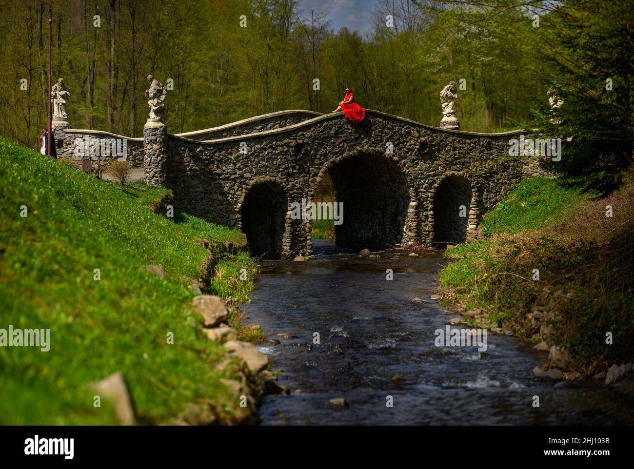 Woiwodschaft, Ukraine 4. Mai 2021: Brücke der vier Evangelisten im Shenborna Park, Frau in einem roten Kleid in der Nähe der Brücke, Kulturpark der Ukraine. Stockfoto