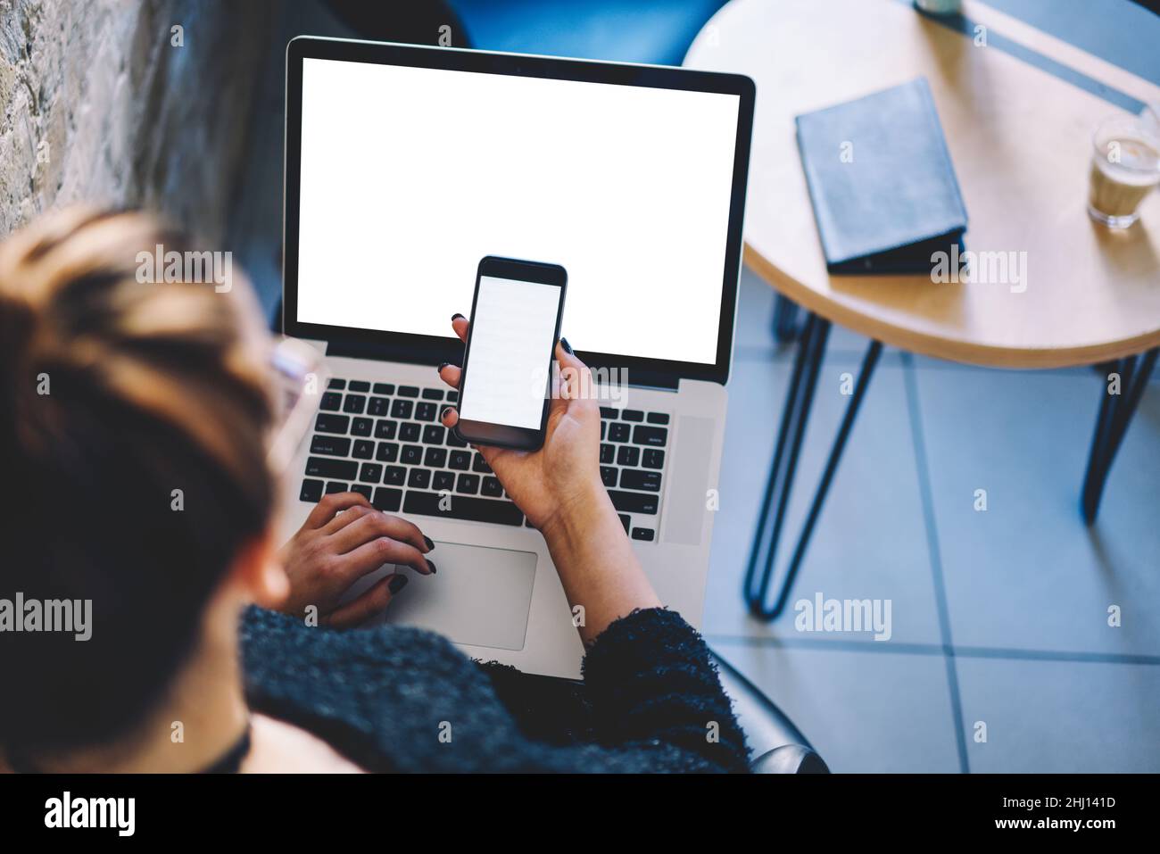 Frau, die in der Cafeteria am Laptop arbeitet und im Mobiltelefon surft Stockfoto