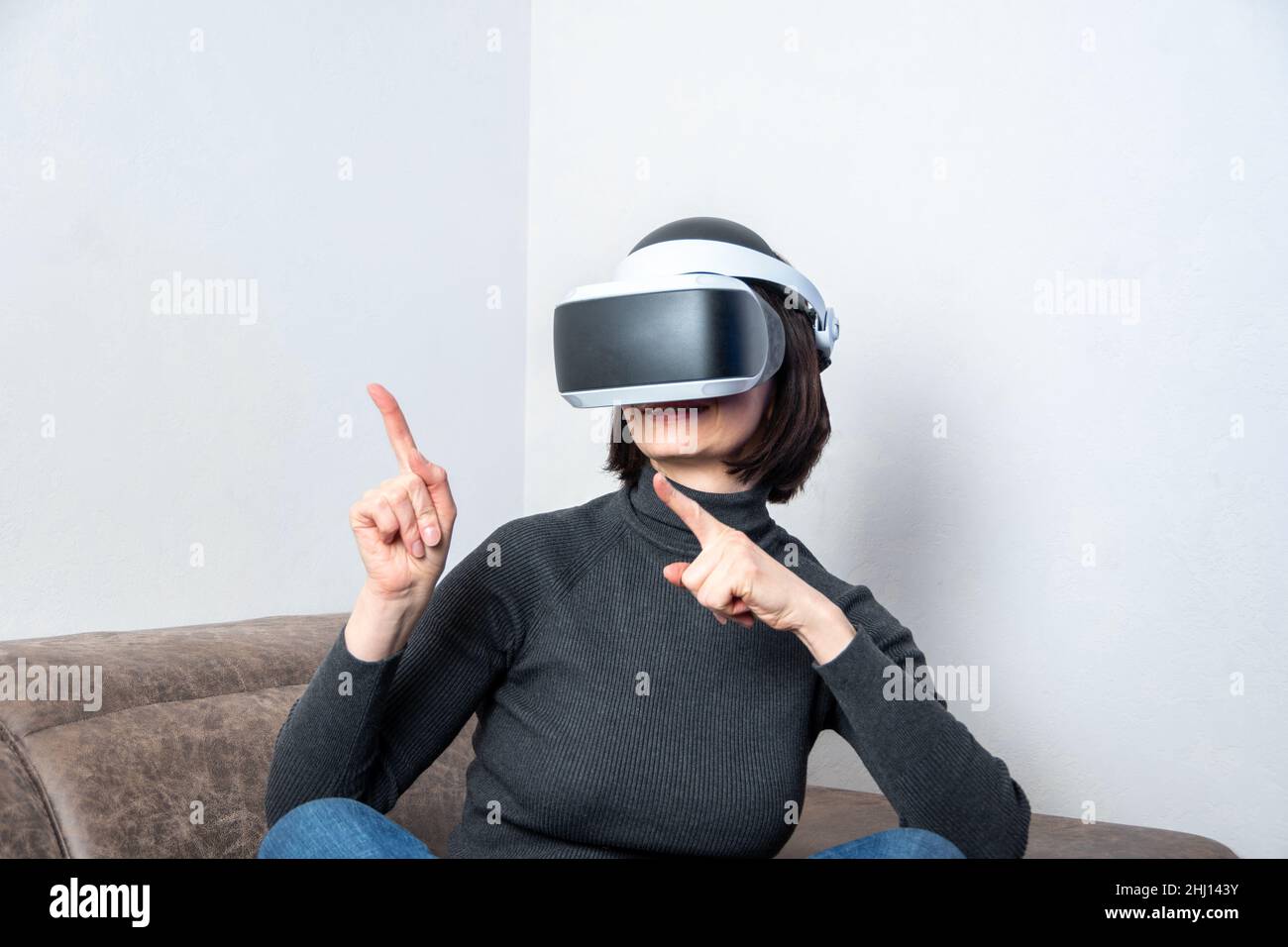 Ein Mädchen in einem Virtual-Reality-Helm zeigt die Finger, macht Handgesten zu Hause. Das Konzept des virtuellen Universums. Lifestyle im virtuellen Raum. Stockfoto