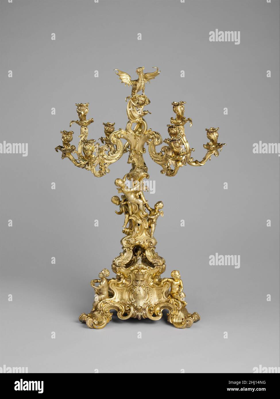 Neun-Licht-Leuchter 1835–36 Paul Storr Britisch Dieses immense Mittelstück ruht auf einem dreieckigen Sockel mit schrägen Seiten und Figuren von Kindern an jeder Ecke und steigt auf eine dreieckige Plattform, an der der eigentliche Leuchter befestigt ist. Drei kräftige, rollende Füße stützen eine zweite Plattform, von der aus ein Schaft aufsteigt, der drei Zweige mit jeweils drei Kerzenarmen unterstützt und insgesamt neun Lichter erzeugt. Durch die Mitte der Kerzenarme ragt eine Gruppe großer Rollen auf, auf denen das Wappen der Familie Herbert steht – ein Wirbel mit ausgebreiteten Flügeln. Der Kerzenständer wurde für Robert Herber angefertigt Stockfoto Neun-Licht-Leuchter 1835–36 Paul Storr Britisch Dieses immense Mittelstück ruht auf einem dreieckigen Sockel mit schrägen Seiten und Figuren von Kindern an jeder Ecke und steigt auf eine dreieckige Plattform, an der der eigentliche Leuchter befestigt ist. Drei kräftige, rollende Füße stützen eine zweite Plattform, von der aus ein Schaft aufsteigt, der drei Zweige mit jeweils drei Kerzenarmen unterstützt und insgesamt neun Lichter erzeugt. Durch die Mitte der Kerzenarme ragt eine Gruppe großer Rollen auf, auf denen das Wappen der Familie Herbert steht – ein Wirbel mit ausgebreiteten Flügeln. Der Kerzenständer wurde für Robert Herber angefertigt Stockfoto