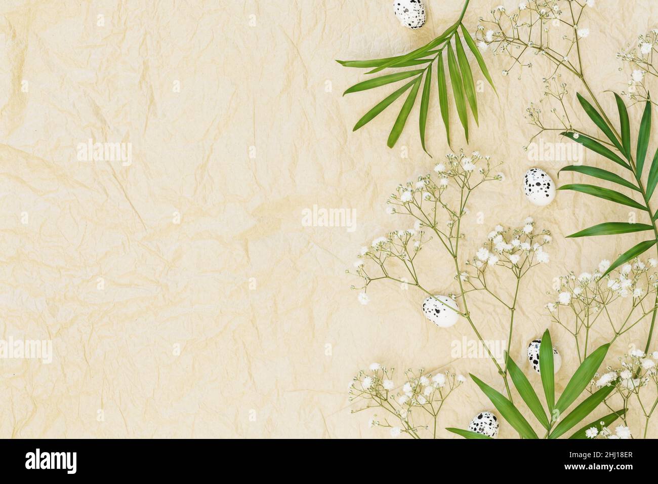 Osterferien Hintergrund. Palmblätter, Eier und Gypsophila-Blumen auf einem handwerklich zerknitterten Papierhintergrund mit Platz für den Text zum Gratulieren Stockfoto