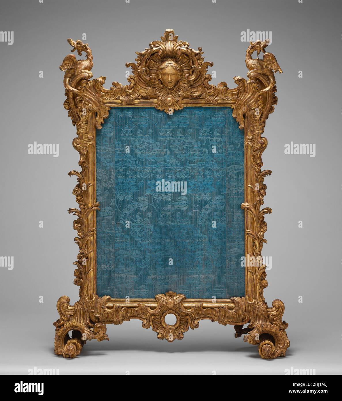 Feuerschutzscheibe ca. 1736–40 vermutlich geschnitzt von Ferdinand Hundt seit dem Mittelalter werden Feuerschutzgitter eingesetzt, um die in der Nähe eines Kamins stehenden oder sitzenden Personen vor der übermäßigen Hitze der offenen Flammen und vor Funken zu schützen. Gegen Ende des siebzehnten Jahrhunderts, Rechteckige Bildschirme mit einem großen zentralen Panel aus buntem Stoff oder anderen kühn kontrastierenden Materialien wurden entwickelt, um die dunkle Öffnung unter dem Mantel zu verbergen, die andernfalls den dekorativen Dado und die getäfelte Dekoration des Raumes unterbrechen würde.[1] die für den Rahmen dieser Bildschirme verwendeten Materialien reichten aus Von wro Stockfoto