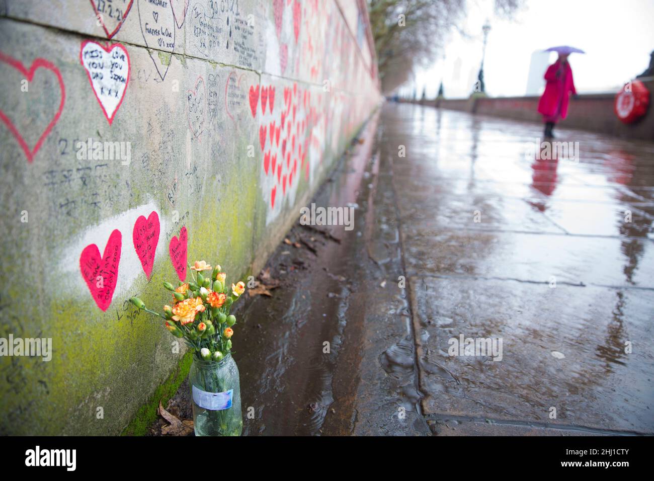 Blumen sind unter rosa Herzen zu sehen, die diejenigen darstellen, die an Covid-19 gestorben sind, an der National Covid Memorial Wall entlang der Themse in London. Stockfoto