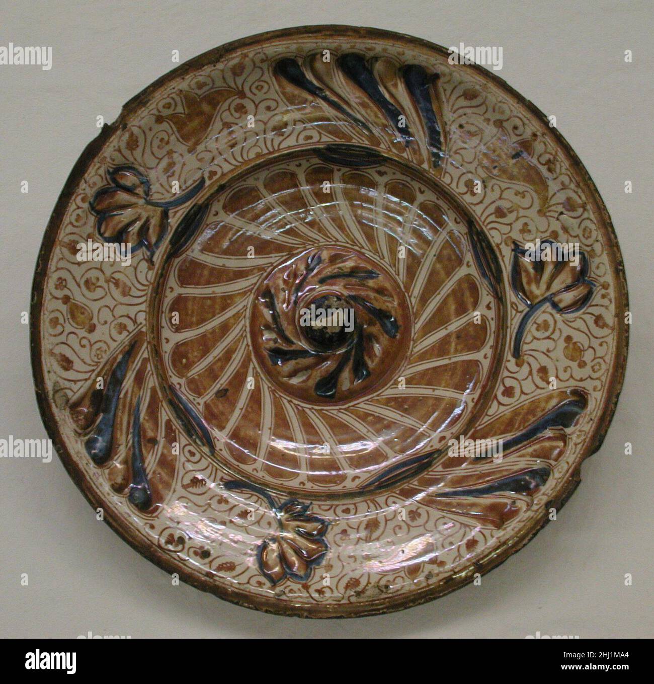 Dish 17th Century Spanish, Valencia Tin-glasierte Steingut, von denen Lusterware eine Art ist, wurde im Nahen Osten im neunten und zehnten Jahrhundert entwickelt, um die Porzellane in China produziert zu imitieren. Die opake weiße Glasur verbarg den Tonkörper, der von hellem Buff bis zu Ziegelrot reichen konnte, was brillante Effekte ermöglichte, indem die weiße Oberfläche mit Metalloxiden bemalt wurde, die zu einer Reihe von Farben abgefeuert wurden. Diese Technik sowie der Einsatz von metallischem Glanz – einer schillernden, kupferfarbenen Glasur – verbreitete sich in der muslimischen Welt und kam in den dreizehn Jahren unter die Töpfer von Valencia Stockfoto