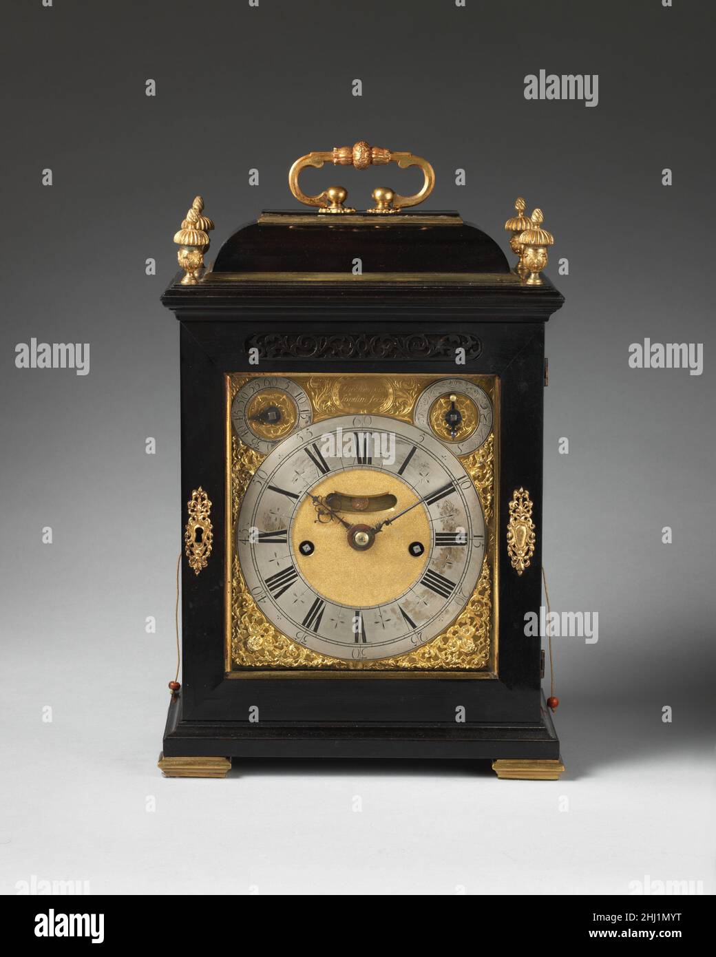 Tisch- oder Halteruhr ca. 1696 Uhrmacher: Thomas Tompion Diese tragbare Uhr hat einen sich wiederholenden Mechanismus, der es erlaubt, auf die Viertelstunde und Stunde zu schlagen, ein wertvolles Merkmal in der Dunkelheit. Abgesehen von Sonderaufträgen waren die Fälle von Tompion-Tischuhren eher nüchtern. Bei der Verwendung von Ebenholz setzte der Uhrmacher auf die angenehme Wirkung der schlichten schwarzen Oberfläche, um den Kontrast zu Gold und Silber des Zifferblatts und der verwendeten Hardware zu bilden (die vaseförmigen Finials wurden von einem späteren Besitzer hinzugefügt). Tischuhr oder Halteruhr. Großbritannien, London. Ca. 1696. Gehäuse: Ebenholz furniert auf Eiche mit vergoldeten und si Stockfoto