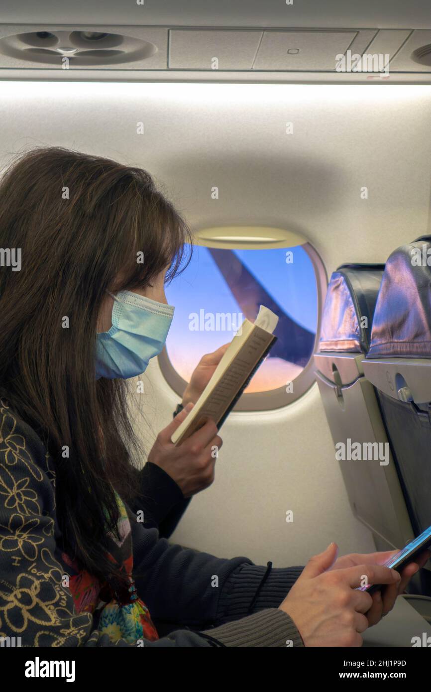 Nette Frau mit Maske im Flugzeugsitz Blick auf Smartphone Stockfoto
