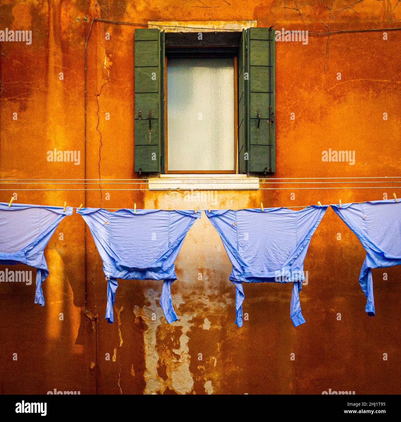 Feb 2020 Venedig - Blaue Hemden, die an einer Wäscheleine an einer verbrannten orangenen Wand und einem versperrten Fenster in Venedig hängen Stockfoto