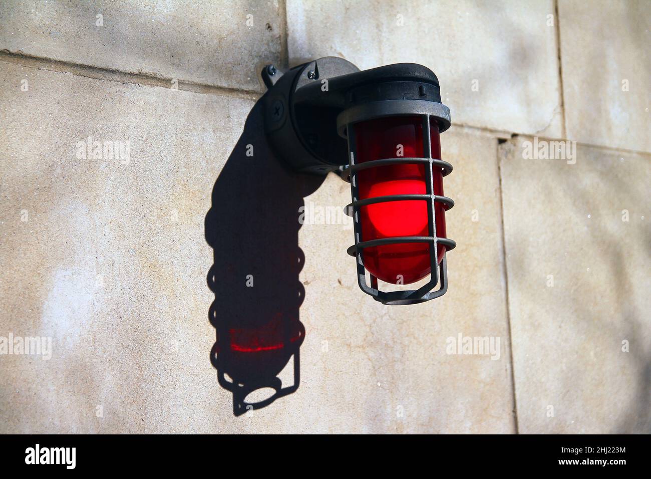 Ein intensives rotes Notlicht an einer Betonwand mit seinem Schatten unter einer heißen Sonne Stockfoto