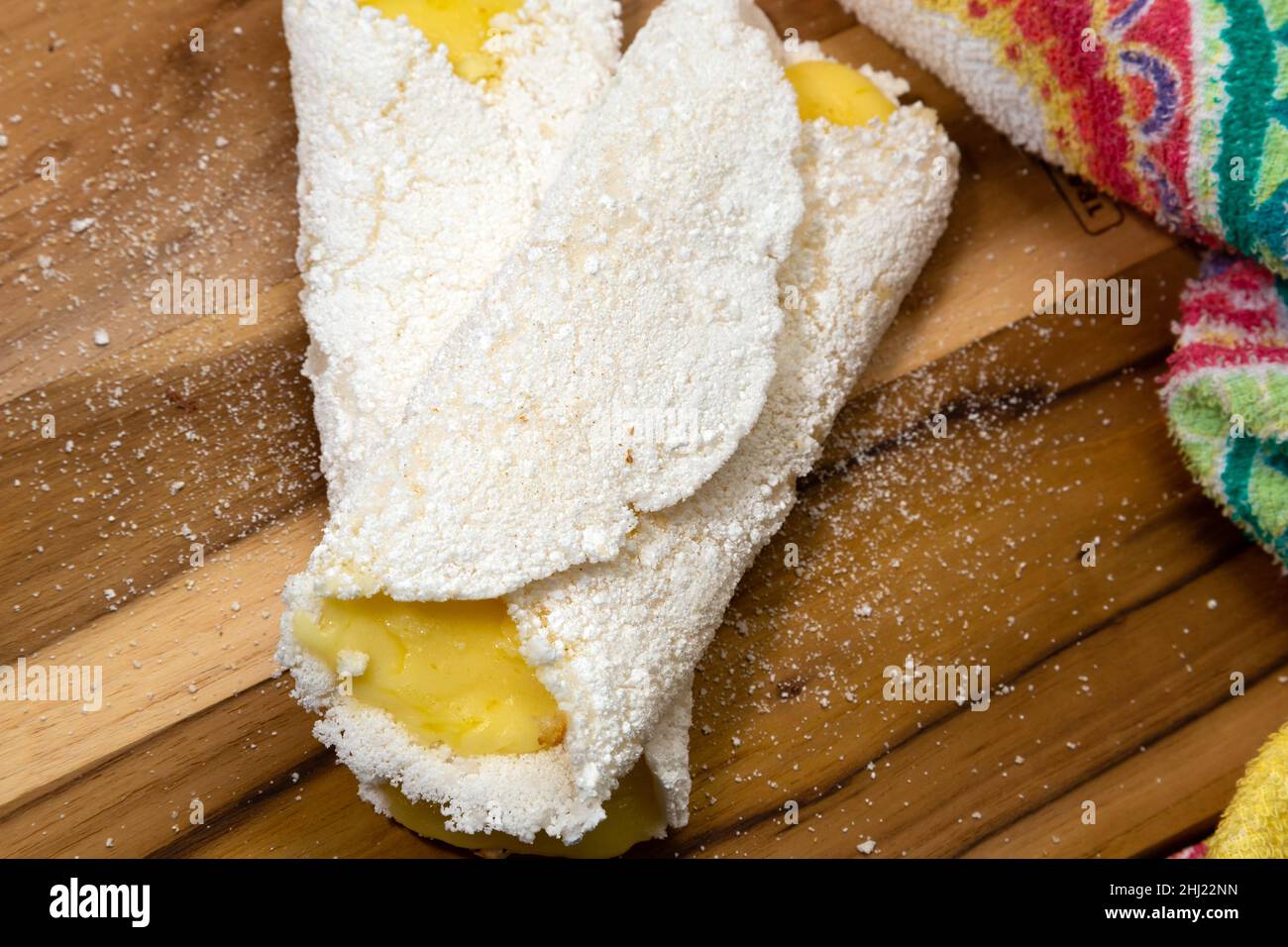 Goiania, Goias, Brasilien – 26. Januar 2021: Zwei Tapiocas gefüllt mit Käse auf einem Holzbrett mit einem gemusterten Stoff Detail. Stockfoto