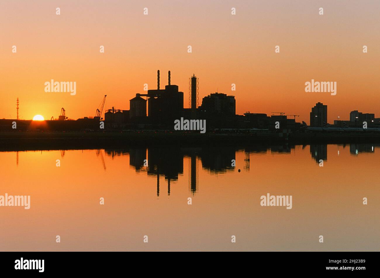 Royal Albert Dock, East London UK, bei Sonnenuntergang, mit dem London City Airport und der Tate & Lyle Fabrik im Wasser reflektiert. Stockfoto