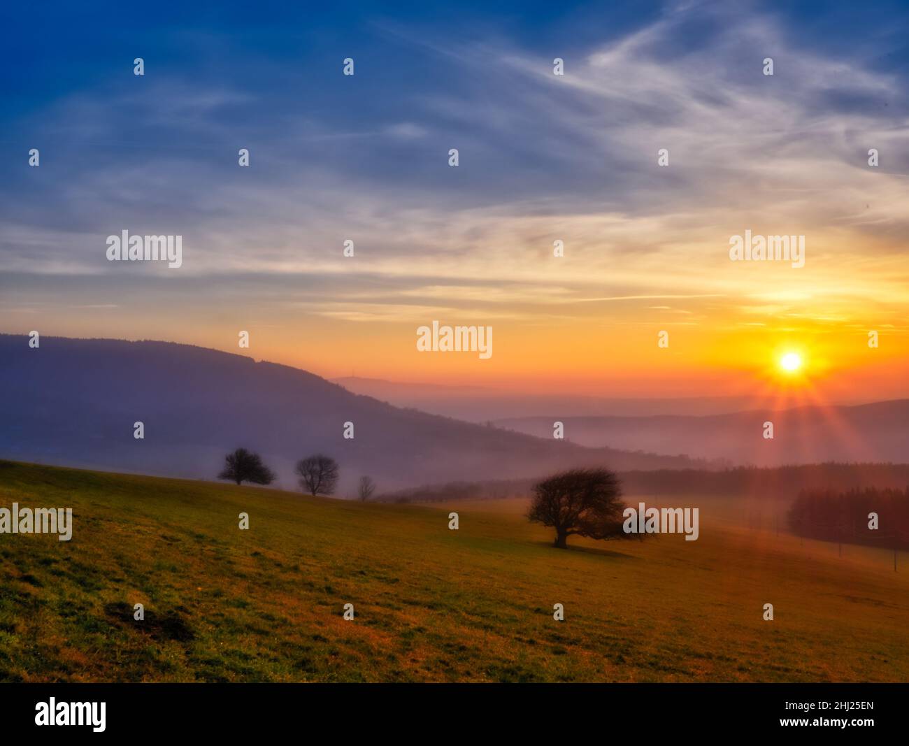 Malerische hügelige Landschaft mit einsamen Bäumen bei Sonnenuntergang, Blick auf das Tal, blauer Himmel mit hohen Wolken, Sonne. Herbstabend. Weiße Karpaten mountai Stockfoto