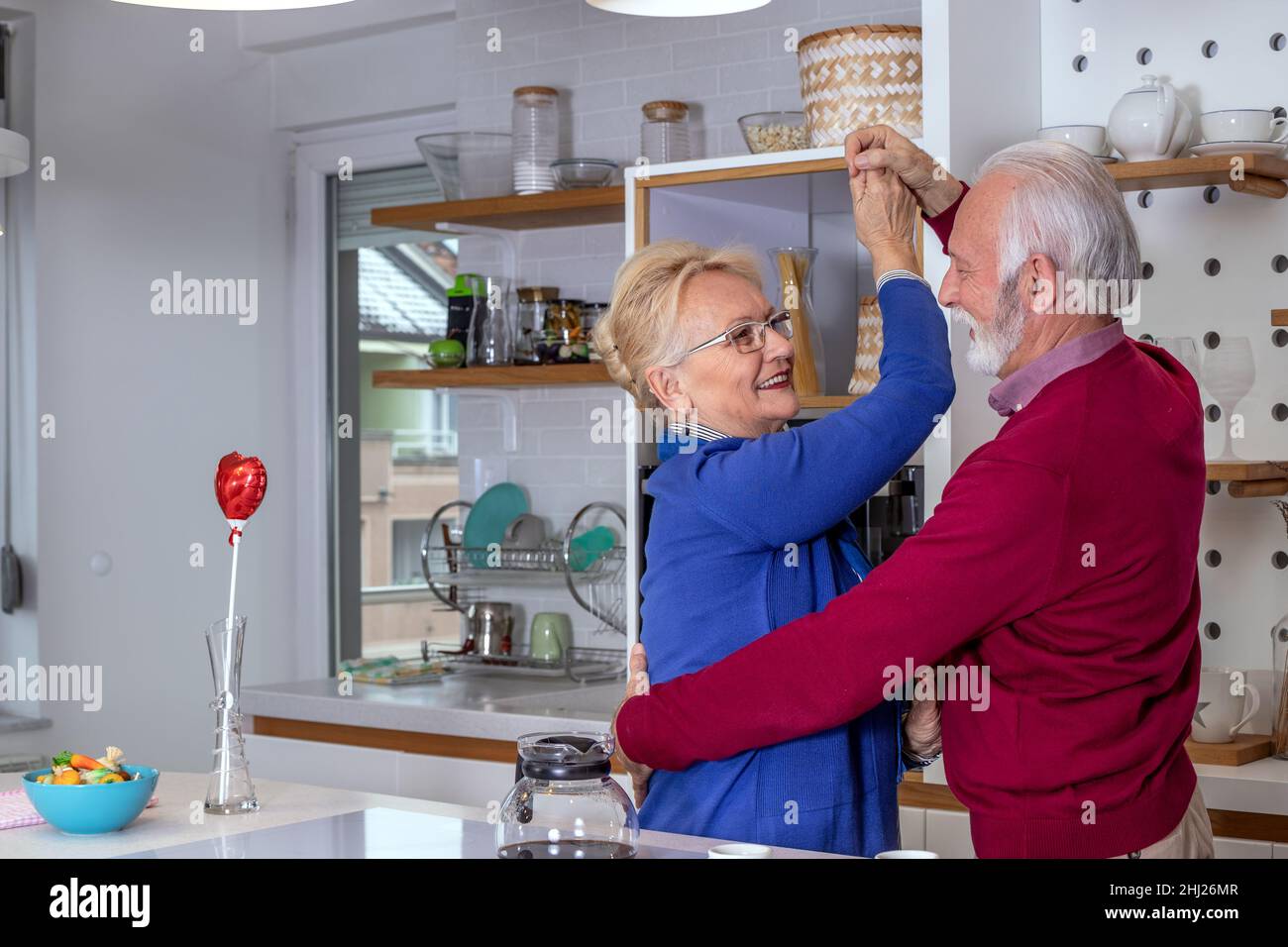 Glückliches Seniorenpaar, das in der Küche tanzt. Der Ehemann gratuliert seiner Frau zum Valentinstag oder zum Hochzeitstag. Stockfoto