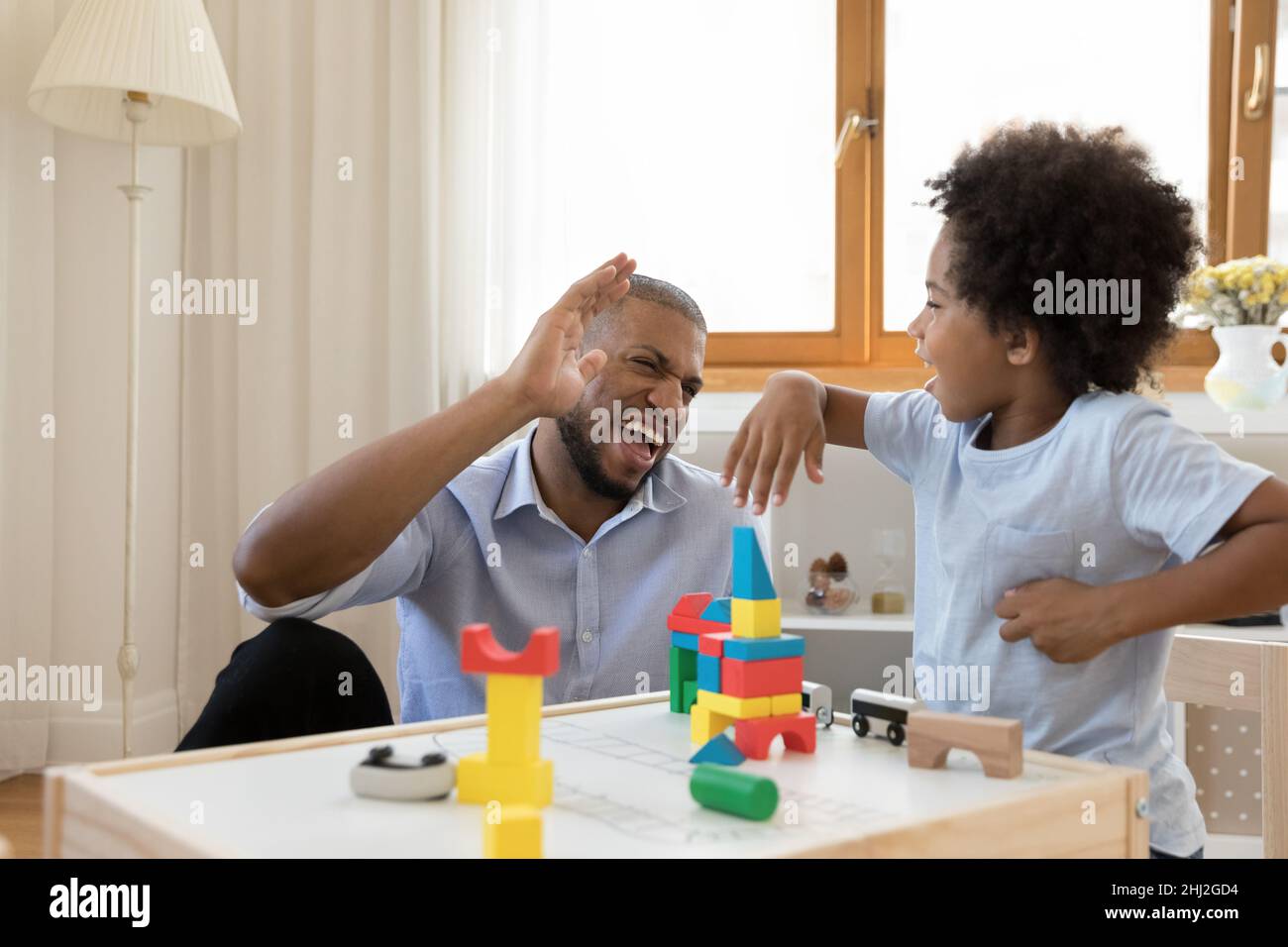 Fröhlicher afrikanischer Vater und Sohn, der zu Hause hoch spielt Stockfoto