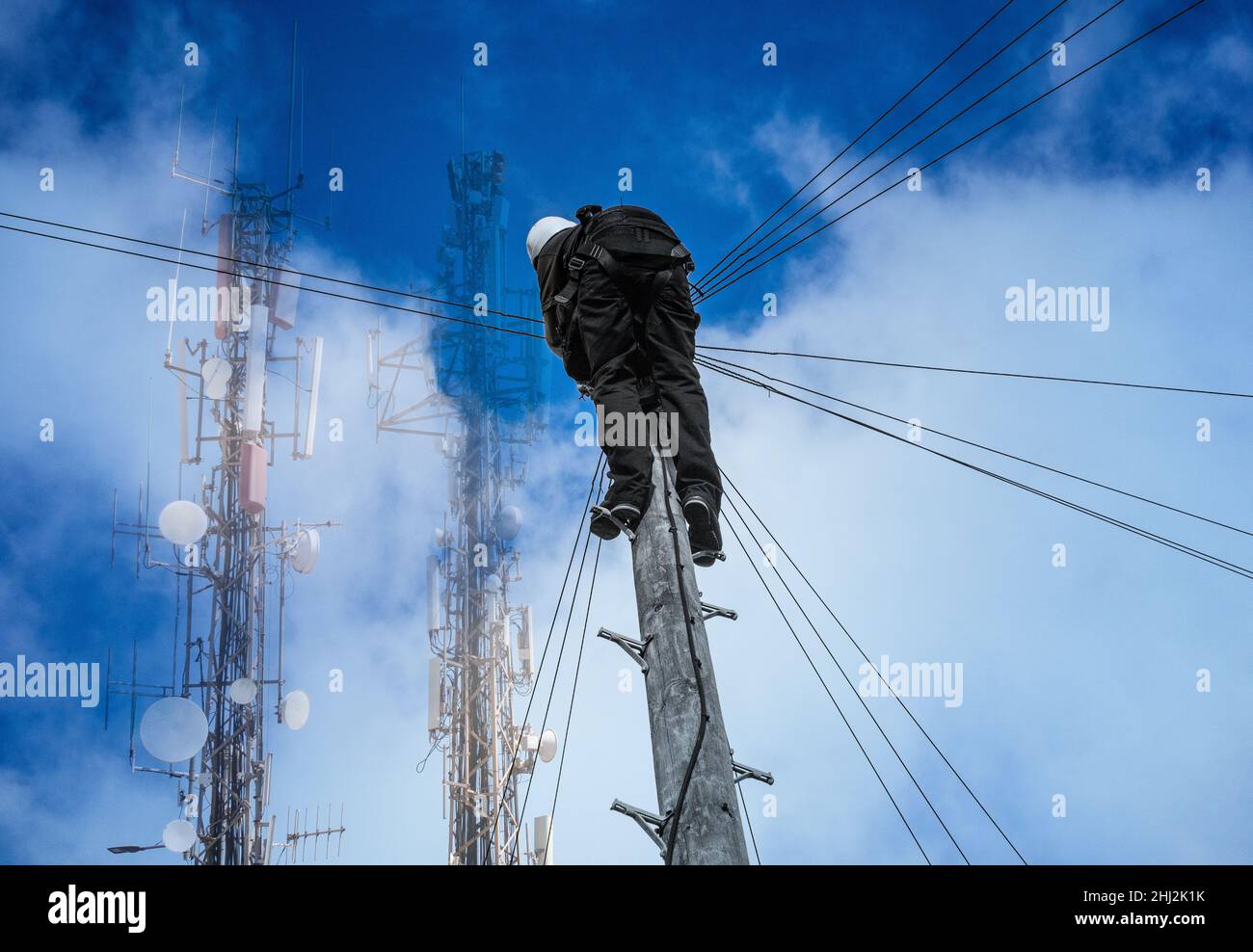 Telekommunikationsingenieur prüft Leitungen am Telegrafenmast mit Antennen im Hintergrund. Breitband, Glasfaser, Internet, 4 5G Stockfoto
