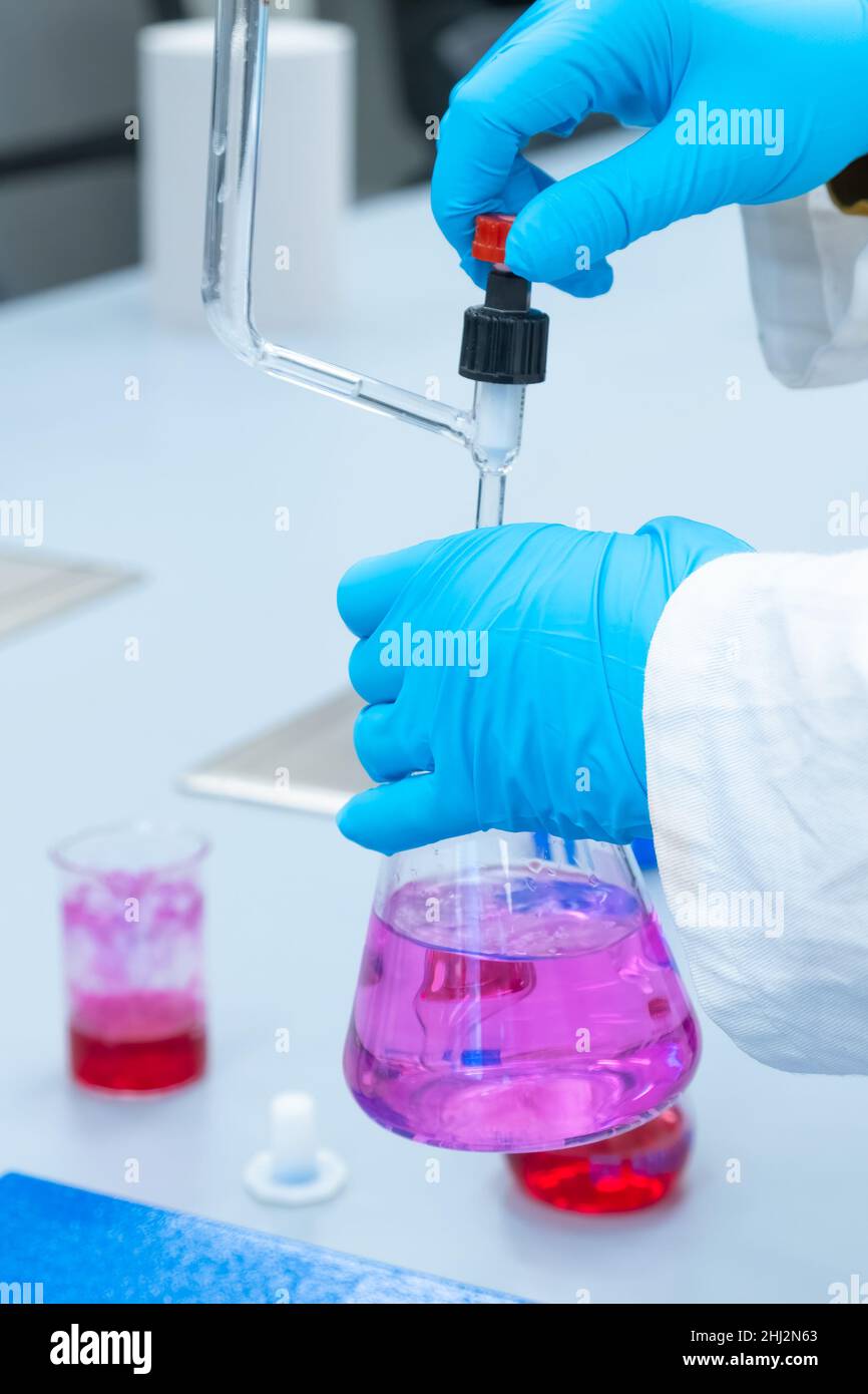 Nahaufnahme Laborarbeiter verwendet eine Titrationsmethode der Analyse, um die chemischen Eigenschaften der Wasserprobe zu untersuchen. Wissenschaftler, der Erlenmeyerkolben mit rosa Lösung hält Stockfoto
