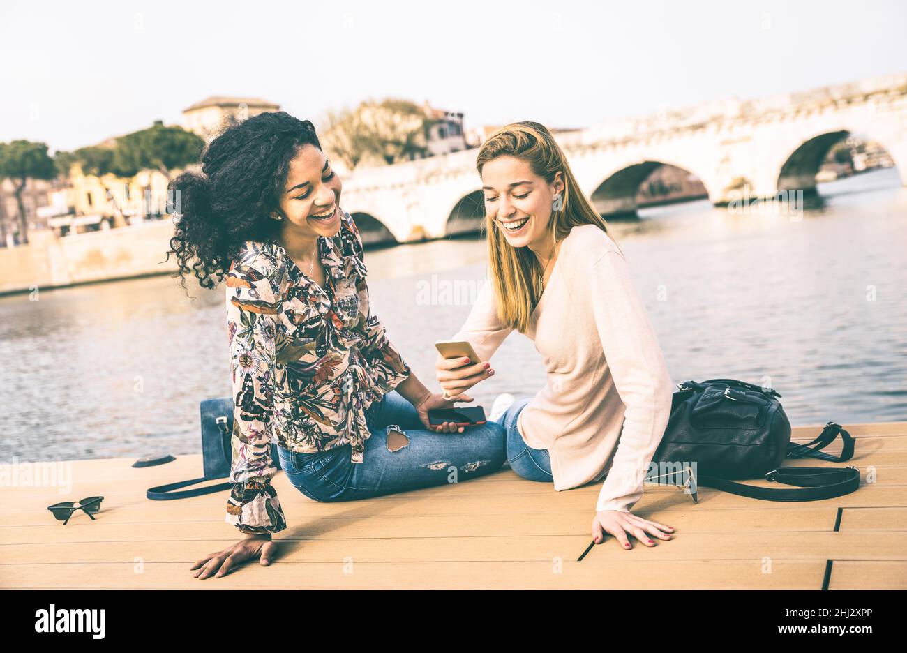 Glückliche multirassische Freundinnen, die Spaß mit Handy im Park haben - Freundschaftskonzept mit Mädchen auf Wanderreisen - moderner weiblicher Lebensstil Stockfoto