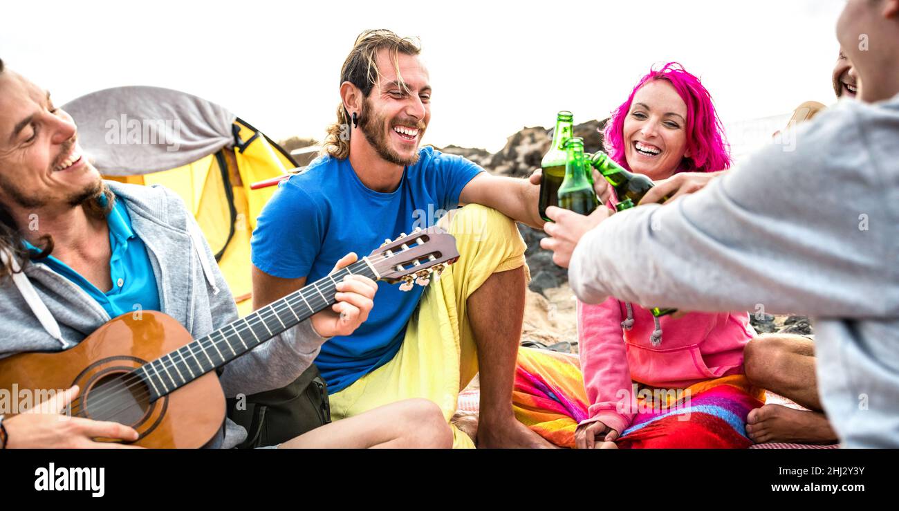 Hippie-Freunde haben gemeinsam Spaß auf der Strand-Campingparty - Lifestyle-Reisekonzept mit jungen Hipster-Reisenden, die Gitarre spielen und Flaschen trinken Stockfoto