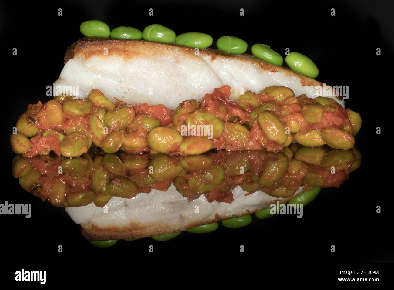 Gebratenes Kabeljaufilet mit einem Ragout aus japanischen Edamamabohnen und Tomaten, Studiofotografie mit schwarzem Hintergrund Stockfoto