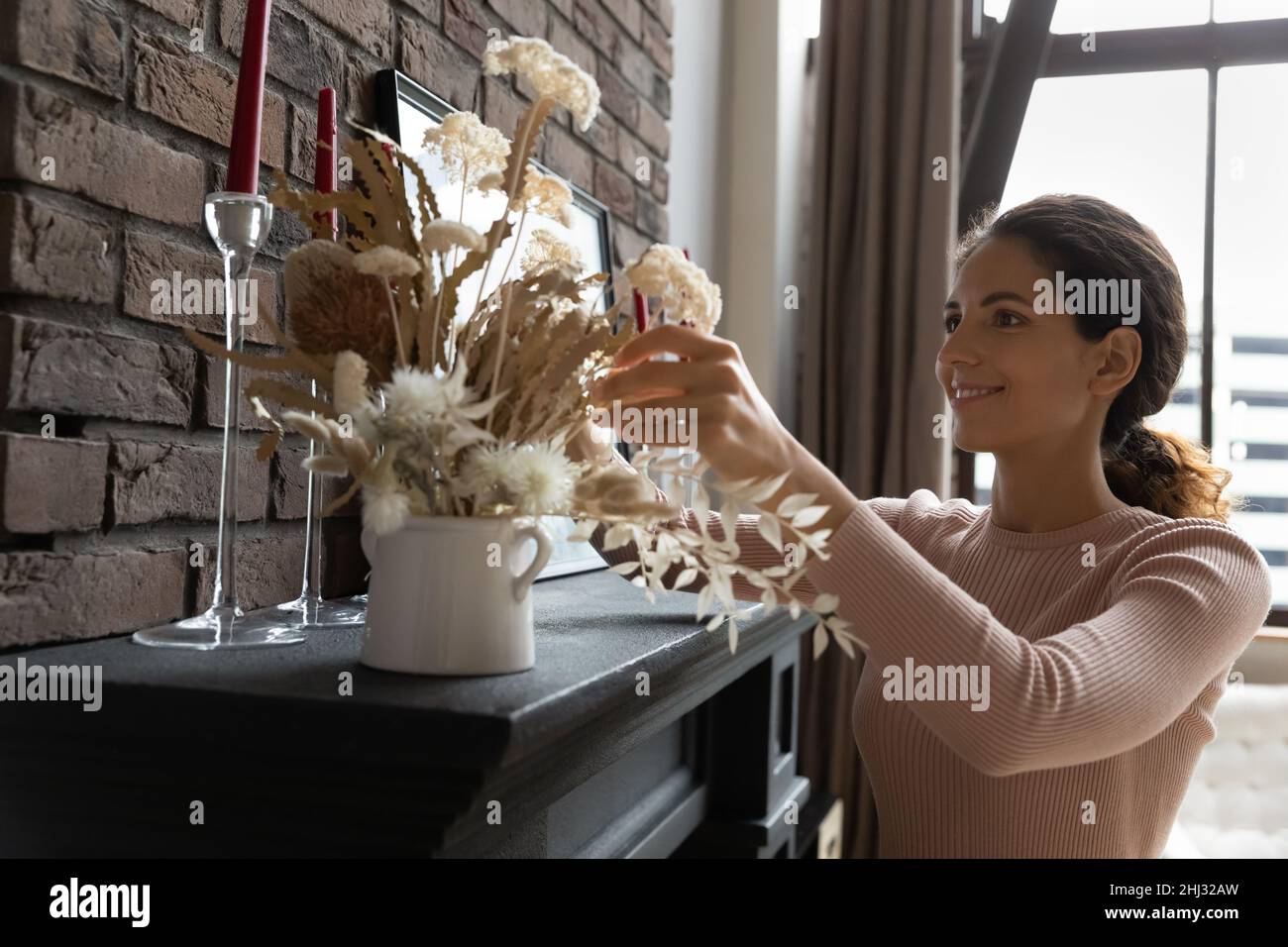 Junge lateinische Hausbesitzerin verbessert die Wohnansicht mit getrockneten Blumen Stockfoto