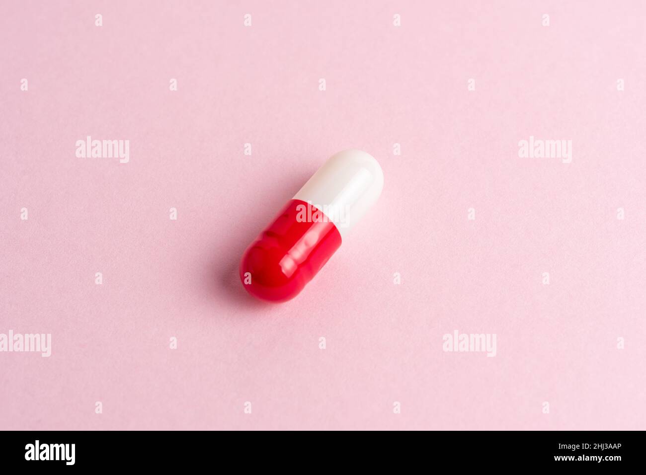 Weiß-rote Kapsel auf einem rosa Hintergrund. Minimales Apothekenkonzept. Flach liegend. Stockfoto