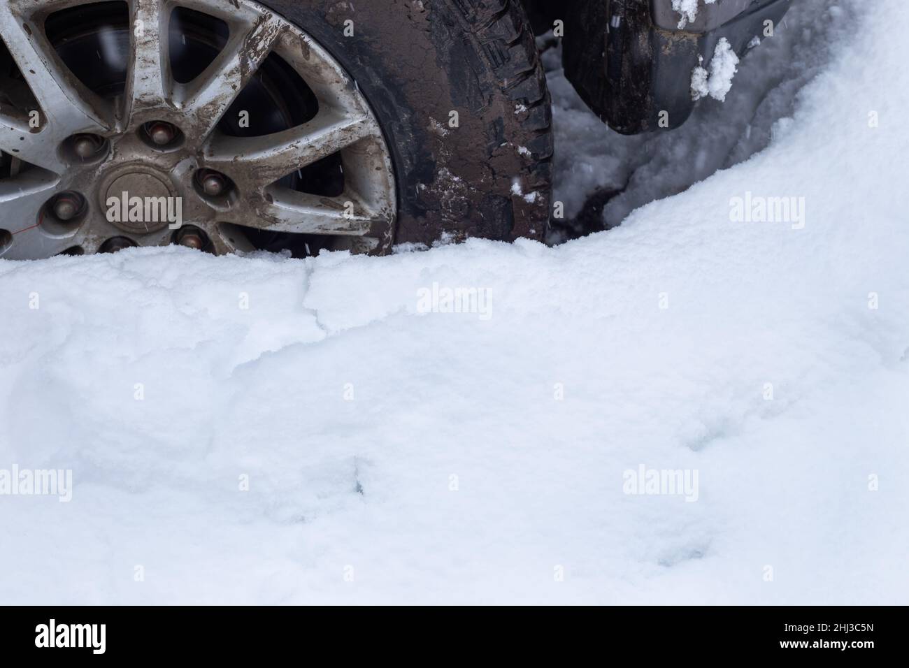 Ein schmutziges Autorad klemmte auf einer schneebedeckten Straße. Schnee driftet im Winter. Stockfoto