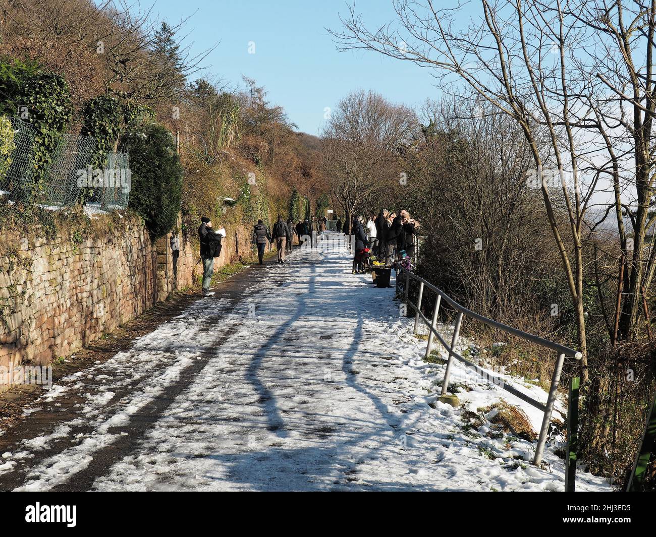 Die Menschen genießen einen sonnigen Wintertag am Philosophenweg in Heidelberg. Die Straße ist mit leichtem Schnee bedeckt. Stockfoto