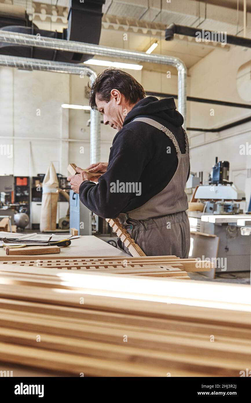 Professioneller Tischler bei der Arbeit, er schnitzt Holz mit einem Holzbearbeitungswerkzeug. Tischlerei und Handwerkskunst Konzept. Vertikale Aufnahme. Seitenansicht Stockfoto