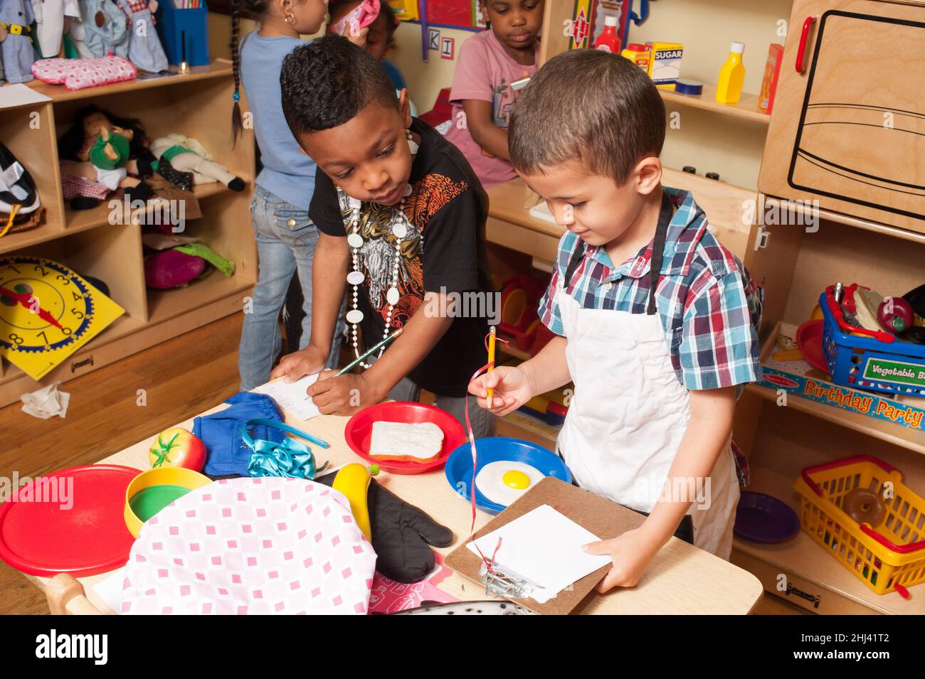 Bildung Vorschule 4-Jährige geben vor, Jungen spielen, die Aufträge für Küche/Koch-Job aufschreiben Stockfoto