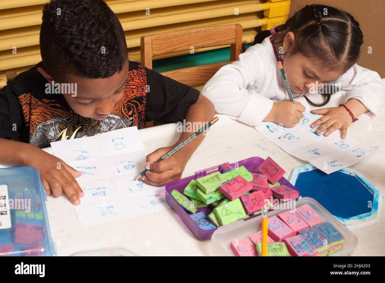 Bildung Vorschule 4-jährige Jungen und Mädchen sitzen nebeneinander Schreiben mit Bleistiften mit gegenüberliegenden Händen Stockfoto