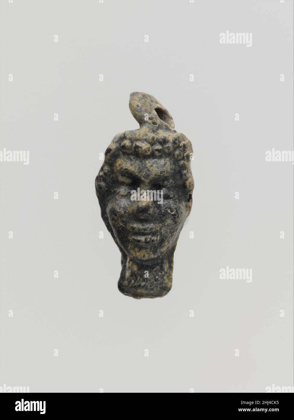 Glasanhänger in der Form eines schwarzen Afrikaners 2nd–1st Jahrhundert v. Chr. griechischer, östlicher mediterraner, ungewisser Farbton, möglicherweise tiefviolett, schwarz wirkend. Massiver, vertikaler Anhänger, mit markanten Schimmelflecken, die an den Seiten des Kopfes und unter dem Hals verlaufen; Eine schlaue Aufhängeschlaufe auf dem Kopf, geformt wie der Kopf eines Schwarzafrikaners. Die meisten Oberflächen sind mit emaillartigen grünlichen Verwitterungen bedeckt. Mit Griff oben; Kopf einer Jugend; opak braun.. Glasanhänger in Form eines schwarzen Afrikaners Kopf 249661 Stockfoto