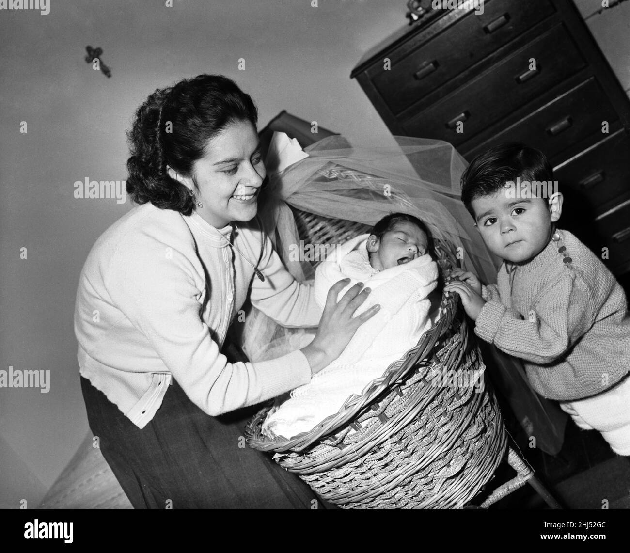 Mrs Myriam Mandragon tuckt Alphonse, während der ältere Bruder Ricardo seine Mutter anschaut und fragt, warum das Baby nicht eine neue Schwester für ihn war, wie er es bestellt hatte. 3rd. Januar 1959 Stockfoto