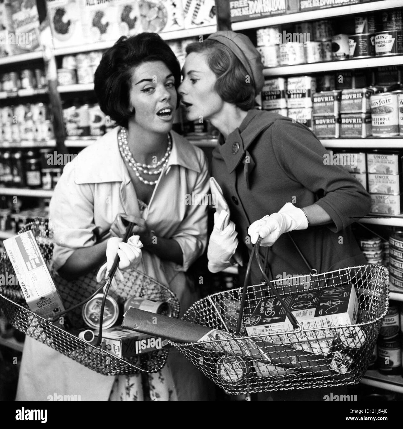 Zwei Frauen flüstern sich im Gang des Ladens zu, 9th. September 1960. „Sie sagen, dass man nicht ohne die Marketingkampagne „New Woman's Mirror“ auskommen kann, um die Einführung von Woman's Mirror, dem „Nachrichtenmagazin für Frauen“, zu fördern. Veröffentlicht 1960-67, im Jahr 1967, wurde es in Schwester Titel Frau verschmolzen. Stockfoto