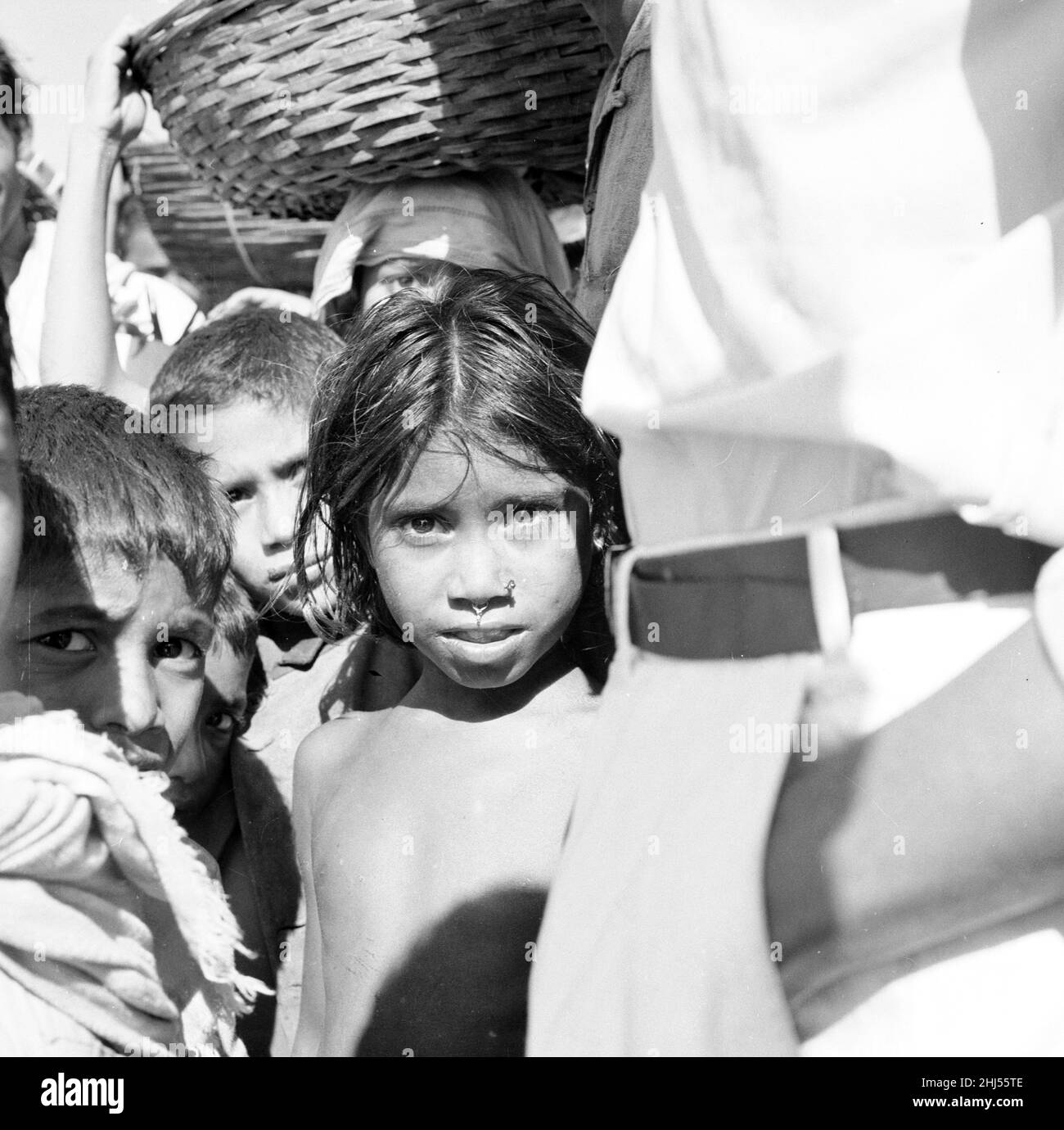 Ein junges Mädchen wartet mit ihren Brüdern und ihrer Schwester, und die lokalen Händler warten darauf, an Bord einer Fähre zu gehen, um sie über den Buriganga River, Dacca, Bangladesch, zu bringen. Februar 1961 l Stockfoto