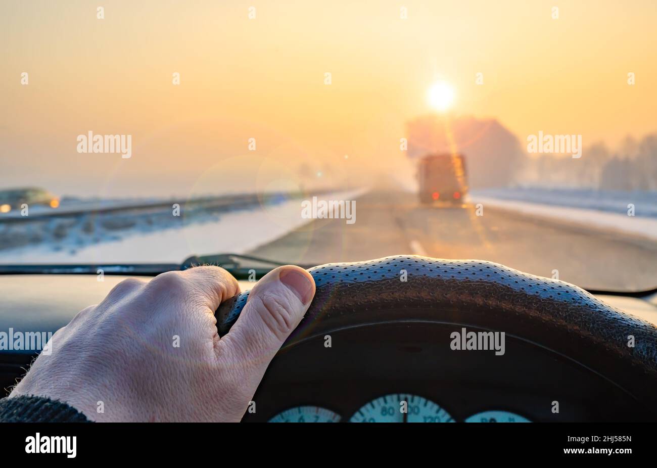 Blick auf die Fahrerhand am Lenkrad eines Autos, das im Verkehrsfluss auf einer Landstraße unterwegs ist, Autobahn im kalten frostigen Winter Stockfoto