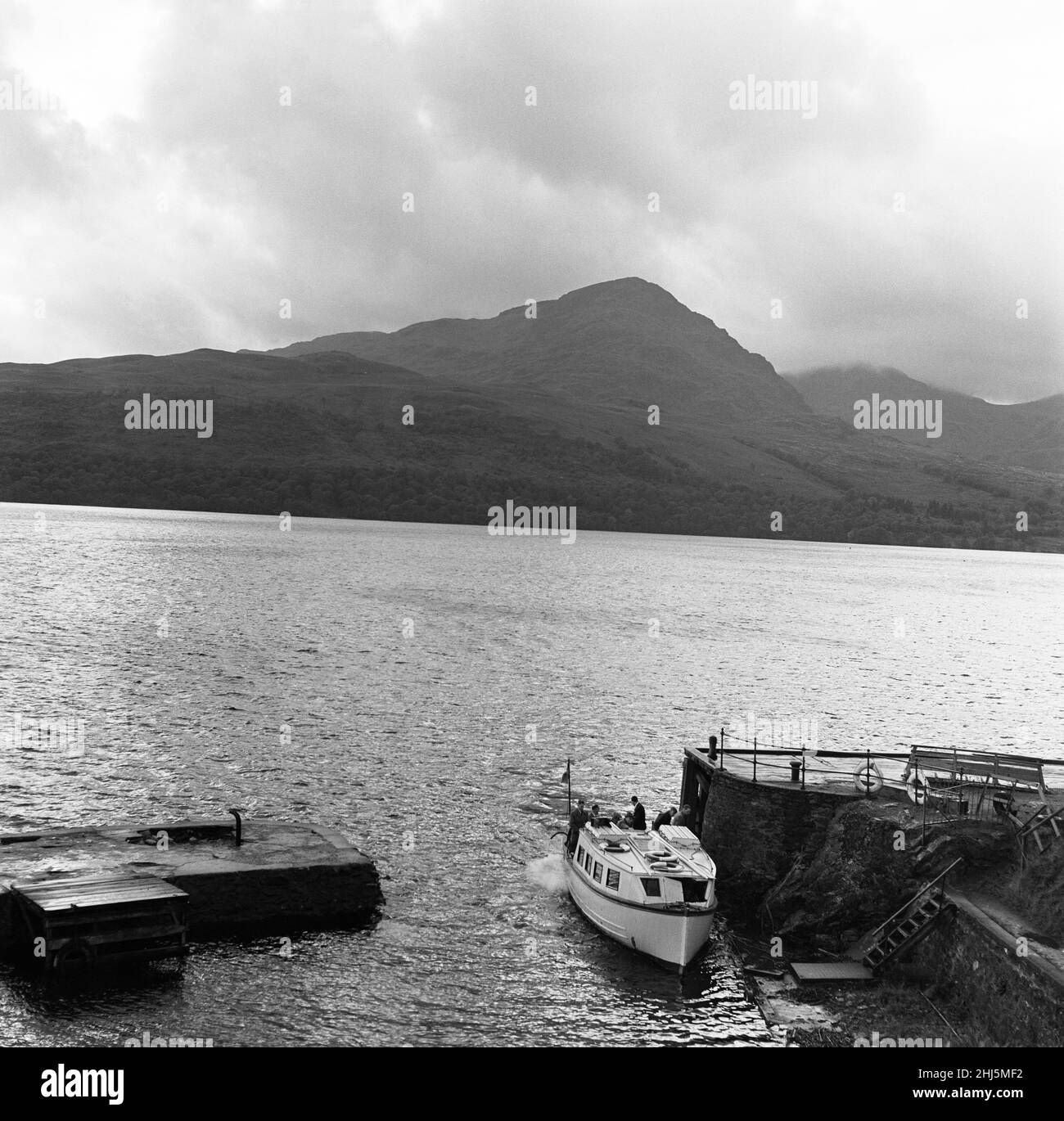 Das kleine Boot schnappt sich mit viel Getue in den Hafen von Inversnaid von der anderen Seite des Loch Lomond. Ben Vane hat sich bereits in die Nacht zurückgezogen, aber silbrige Lichtwellen fallen auf den Loch und man hat das Gefühl, dass alles gut ist und der Tag gut in Schottlands mystischer Landschaft verbracht wird. Inversnaid, Stirling, Schottland. 7th. November 1956. Stockfoto