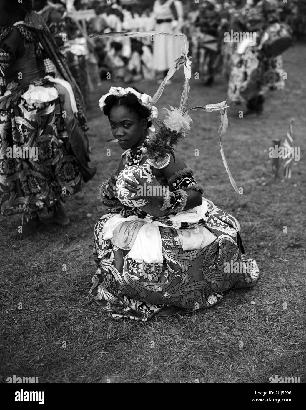 Eine nigrische Tänzerin aus dem Stamm der Efik hält am Ende eines traditionellen Tanzes für die Königin und den Herzog von Edinburgh während ihrer Royal Tour. Die Ntimi ist der höchste zeremonielle Tanz der Frauen von Calabar und wird nur bei großen öffentlichen Anlässen aufgeführt. Zwei wichtige Gegenstände des Kostüms sind die rote Feder, die zwischen den Lippen gehalten wird, um für Stille zu sorgen, und ein Kürbis, der kunstvoll manipuliert wird, um Botschaften der Loyalität zu vermitteln. . Calabar, Nigeria. 8th. Februar 1956. Stockfoto