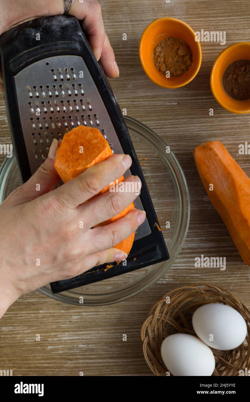 Frau Hände reiben Karotte auf Reibe für Karottenkuchen auf Holz Hintergrund Stockfoto
