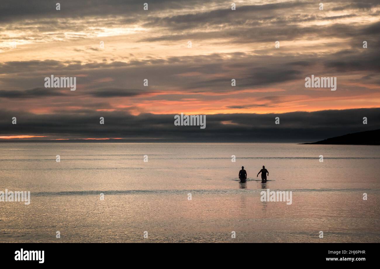 Fountainstown, Cork, Irland. 27th. Januar 2022. Miriam Spilland und Aoife O'Donovan waten in das Meer, während sie vor der Morgendämmerung an einem ruhigen Wintermorgen in Fountainstown, Co. Cork, Irland, schwimmen gehen. Kredit: David Creedon / Alamy Live Nachrichten Stockfoto