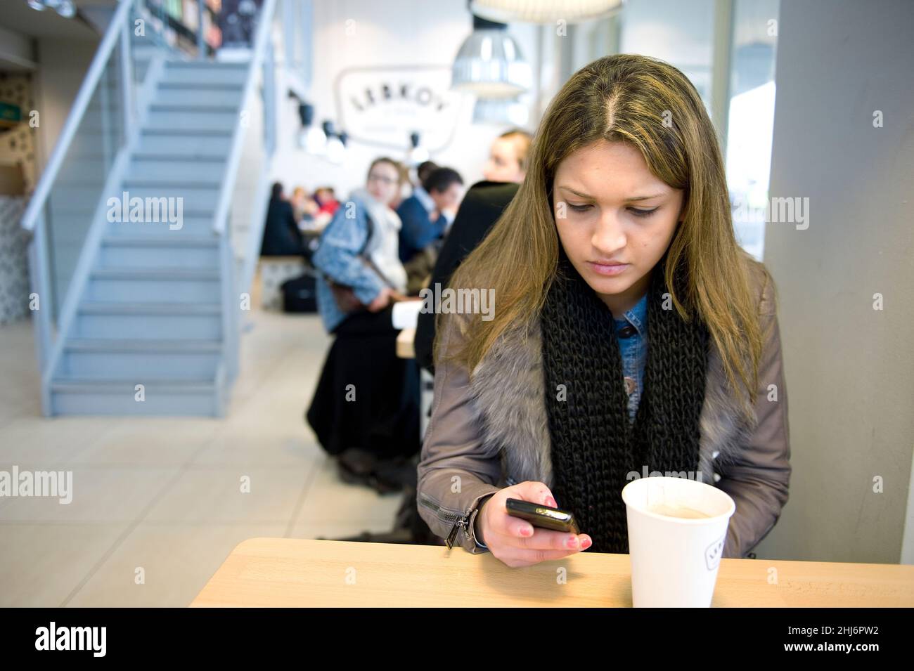 Rotterdam, Niederlande. Junge Erwachsene Frau, die ihre Smartphone-Nachrichten abcheckt, während sie einen Kaffee im Lebkov Coffee Place trinken. Stockfoto