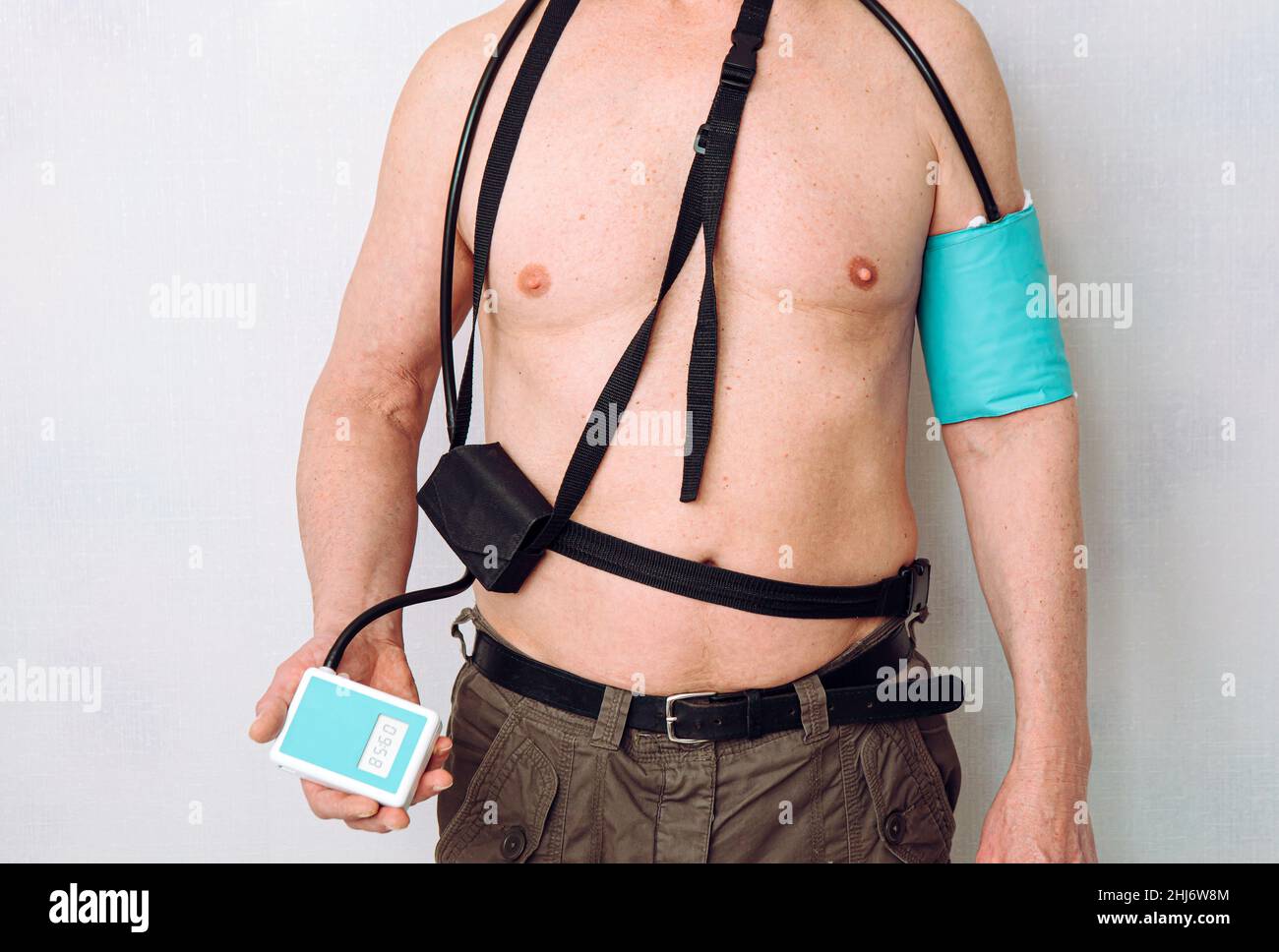 Körper eines Mannes mittleren Alters, der einen tragbaren ambulanten Blutdruck-Monitor (ABPM) zur Messung bei normalen täglichen Aktivitäten zu Hause verwendet. Stockfoto