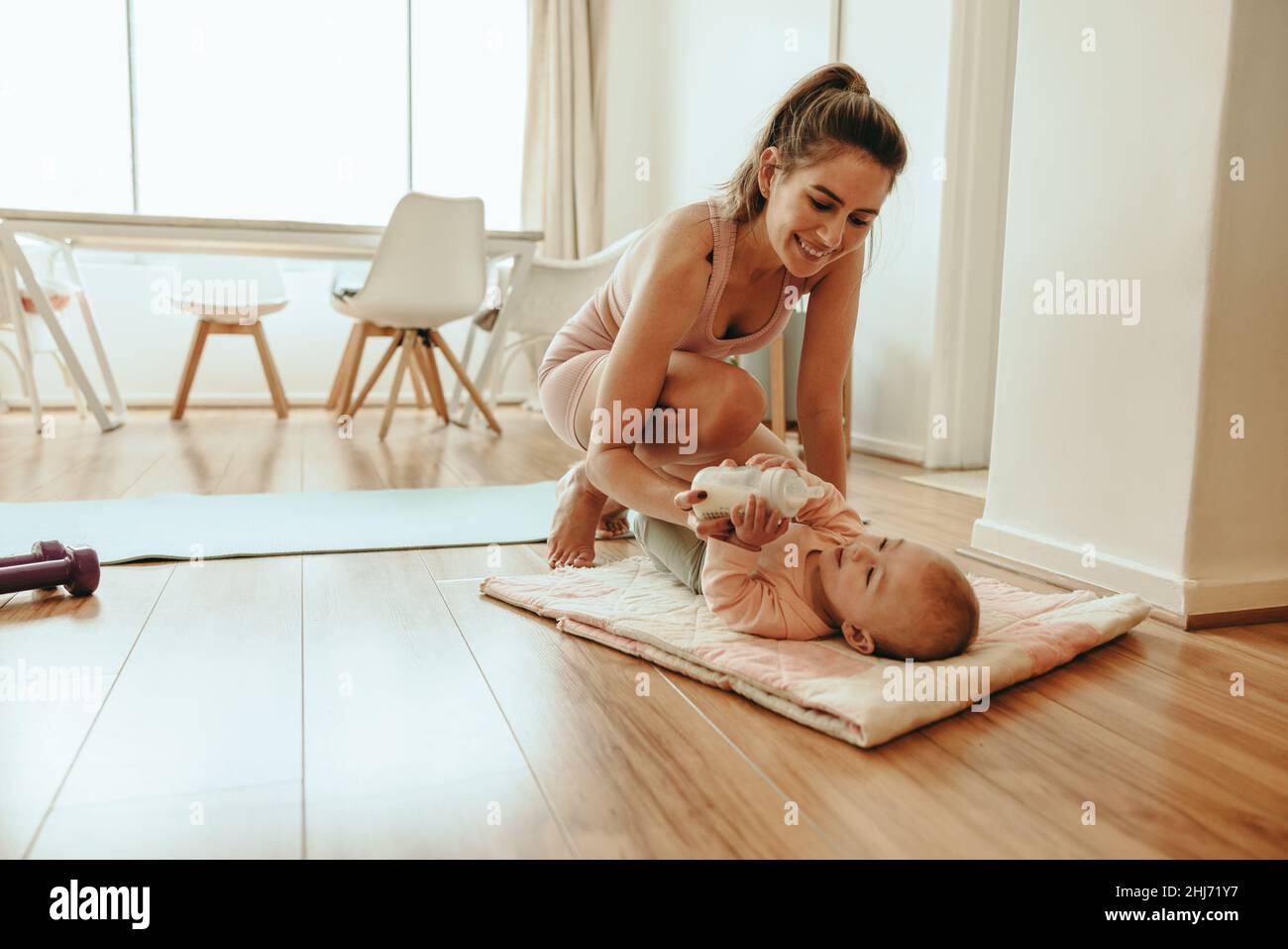 Yogi-Mutter füttert ihr Baby zu Hause mit einer Flasche Milchpulver. Glückliche neue Mutter, die sich um ihr neugeborenes Baby kümmert, während sie eine Pause vom Arbeiten macht. Einzeln Stockfoto