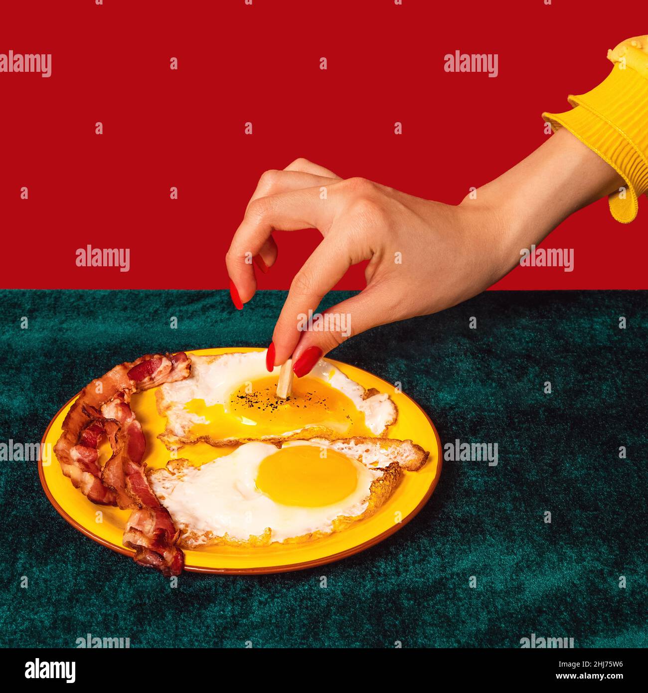 Nahaufnahme von Mädels Hand schmeckender Speck und Eier auf grünem und rotem Hintergrund isoliert. Interieur im Retro-Stil. Food Pop Art Fotografie. Stockfoto