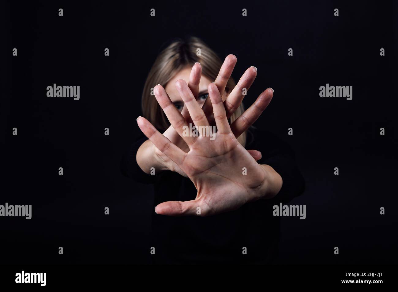 Weibliche Person mit den Händen vor ihr zeigt Stop-Zeichen versteckt Gesicht in schwarzem Kleid auf schwarzem Hintergrund. Opfer von körperlicher und psychischer Misshandlung Stockfoto