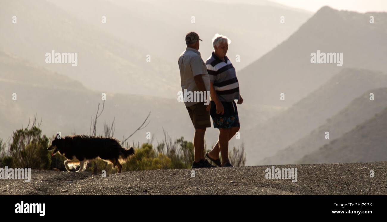 Laingsburg, Südafrika - zwei unbekannte Freunde und ihr Hund treffen sich auf einem Hügel mit Blick auf ein sonnenüberflutetes Tal Stockfoto