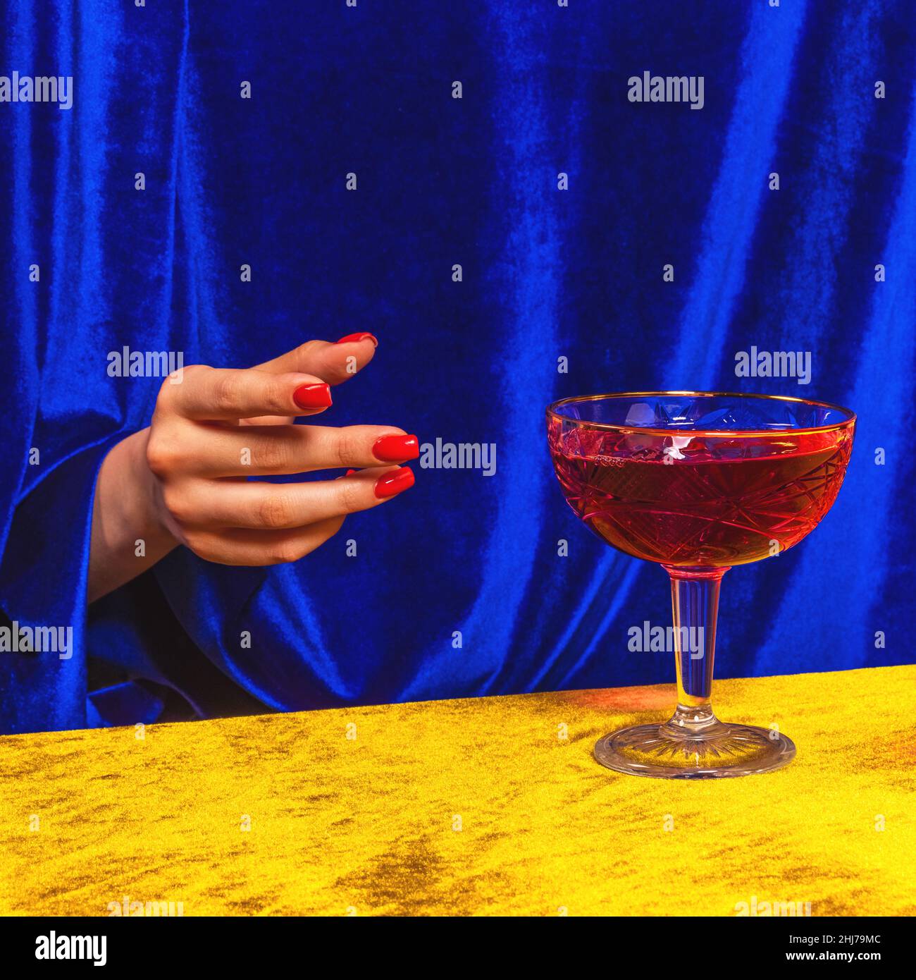 Weibliche Hand greift nach Glas mit manhattan-Cocktail isoliert auf hellgelb-blauem Neon-Hintergrund. Konzept des Geschmacks, alkoholische Getränke Stockfoto