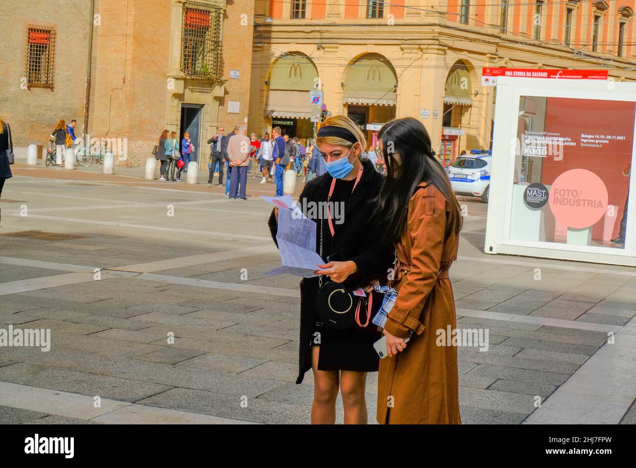 Oktober 2021 Bologna, Italien: Zwei junge Frauen in stilvoller Kleidung tragen medizinische Gesichtsmasken und studieren den Stadtplan in der Nähe des Neptunbrunnens auf dem Stockfoto